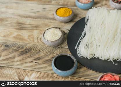 soya sauce raw rice turmeric bowl near dried rice noodles black tray wooden texture background