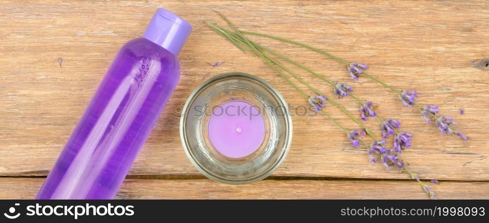 SPA accessories: lavender shampoo, scented candle, dried lavender flowers on a wooden background.
