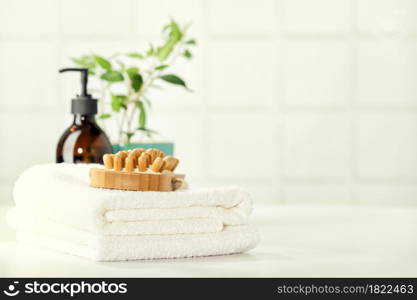 SPA and Bathroom accessories on white bathroom countertop against tile wall - Amber glass bottles, wooden massage brush, house plant, towels, green jade roller. Natural organic eco cosmetic packaging, luxury beauty products for body care