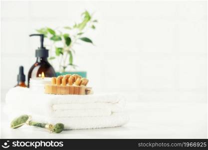 SPA and Bathroom accessories on white bathroom countertop against tile wall - Amber glass bottles, wooden massage brush, house plant, towels, green jade roller. Natural organic eco cosmetic packaging, luxury beauty products for Lymph drainage and lymph massage