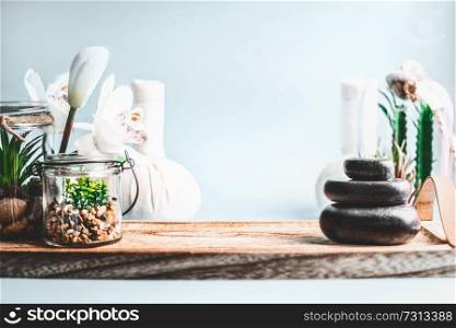 Spa background. Stack of hot stones setting, wellness equipment with succulent plants and white orchid flowers on table at light blue wall background. Beauty, healthy lifestyle and body care concept.