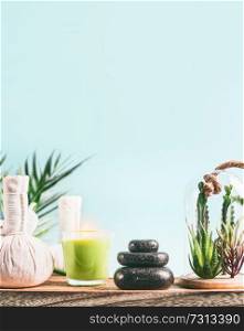 Spa background with massage equipment:  stack of massage stones,  aromatherapy candles,  herbal stamps setting on wooden table with succulent plants at light blue background. Wellness treatment