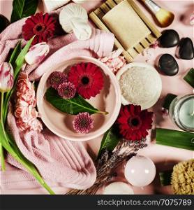 Spa background with sea salt, bowl ,flowers, water, soap bar, candles, essential oils, massage brush and flowers,top view. Flat lay. Pink background