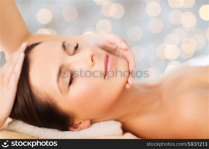spa, beauty, people and body care concept - beautiful woman getting face treatment over holidays lights background