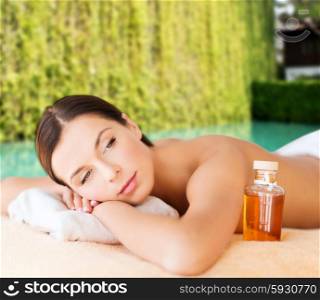 spa, beauty, people and body care concept - happy woman lying on the massage desk with oil bottle over green natural background