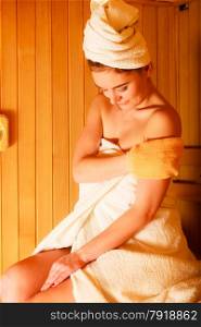 Spa beauty treatment and relaxation concept. Woman white towel relaxing in wooden sauna room, making massage with exfoliation glove