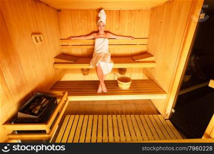Spa beauty well being and relax concept. Woman in full length white towel sitting relaxed in wooden sauna