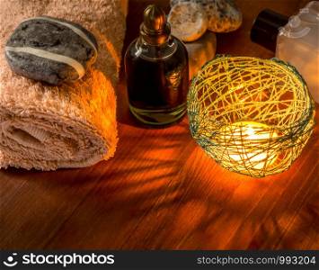 Spa composition with a burning candle bottles with oils, a towel and gray stones. Towel, oil bottles, spa stones on wooden background