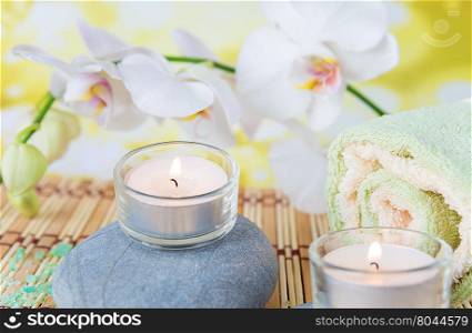 Spa concept: bath towels, two lighted candles on a wild rock and a branch of white orchid