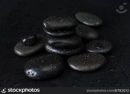 Spa concept with heap of the black basalt massage stones covered with water drops on a black background