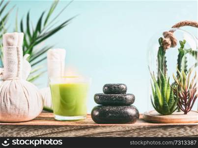 Spa concept with massage equipment: stack of massage stones, aromatherapy candles, herbal stamps setting on wooden table with succulent plants at light blue background. Wellness treatment