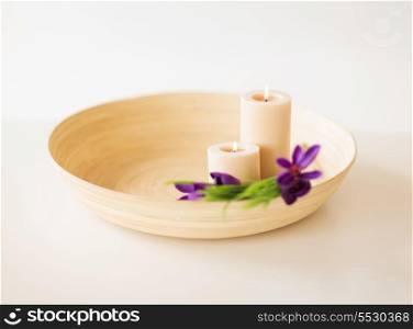 spa, health and beauty concept - candles and iris flowers in wooden bowl