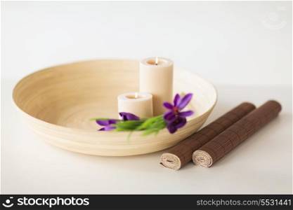 spa, health and beauty concept - candles and iris flowers in wooden bowl and bamboo mat