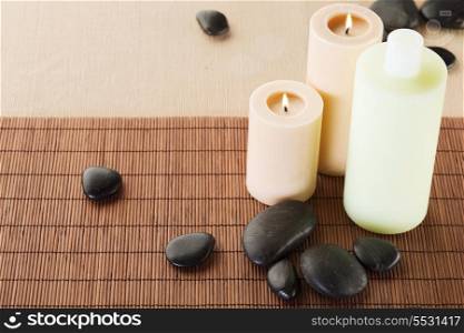 spa, health and beauty concept - closeup of shampoo bottle, massage stones and candles