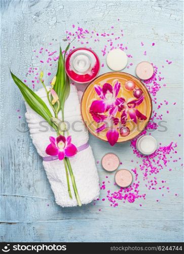 Spa or wellness setting with towel, bamboo leaves , bowl with pink orchid flowers and water , cream, candles and sea salt on light blue shabby rustic background, top view