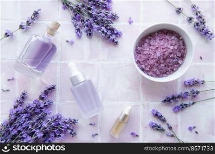 Spa products and lavender flowers on a pink tile background.  Aromatherapy lavender bath salt and massage oil