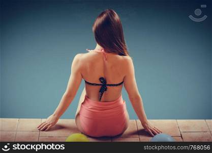 Spa relax and holidays concept. Attractive woman in swimsuit back view. Fit female body, girl sitting at poolside