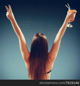 Spa relax and holidays concept. Happy woman in swimsuit back view. Fit female body, girl long hair at poolside with cocktail glass arms raised up in celebration