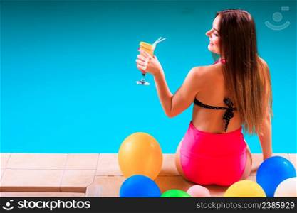 Spa relax and holidays concept. Young woman in swimsuit rear view. Fit female body, girl sitting at poolside holding cocktail glass in hand