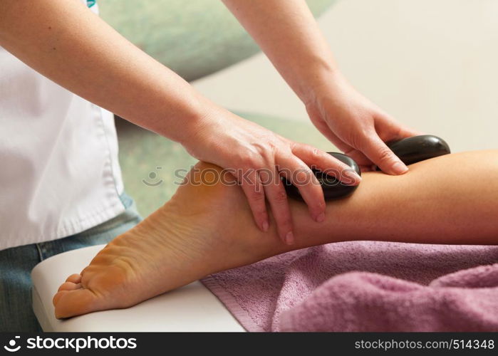 Spa relaxation, healthy pleasure concept. Woman lying on stomach, female masseuse doing legs and feet massage with hot stones. Masseuse doing legs massage with hot stones