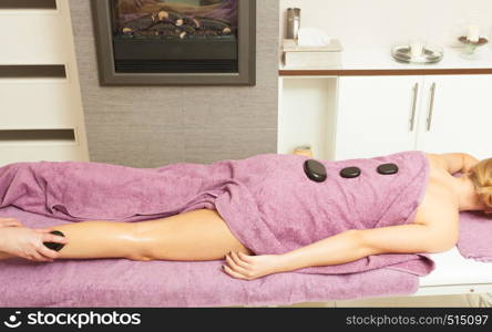 Spa relaxation, healthy pleasure concept. Woman lying on stomach, female masseuse doing legs and feet massage with hot stones. Masseuse doing legs massage with hot stones