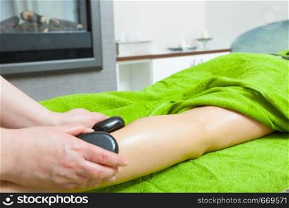 Spa relaxation, healthy pleasure concept. Woman lying on stomach, female masseuse doing legs and feet massage with hot stones. Masseuse doing legs massage with hot stones