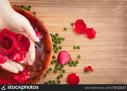 Spa Salon: Beautiful Female Hands with French Manicure in the Bamboo Bowl of Water with Red Roses and Rose Petals on the Straw Mat