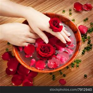 Spa Salon: Beautiful Female Hands with French Manicure in the Bamboo Bowl of Water with Red Roses and Rose Petals on the Straw Mat