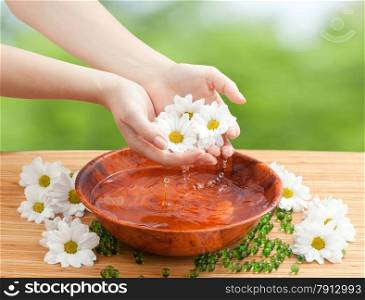 Spa Salon: Beautiful Female Hands with French Manicure in the Bamboo Bowl of Water Holding White and Yellow Flowers on the Straw Mat at the Nature Background