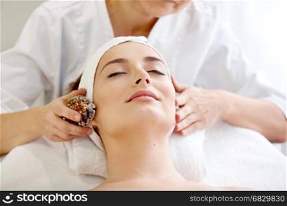 Spa salon: Beautiful Young Woman having Facial Treatment in Spa salon with Sea Shell.