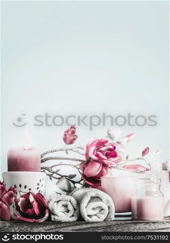 Spa setting arrangements with body care cosmetic products, candles, pink flowers and towels at light blue background with copy space. Healthy still life
