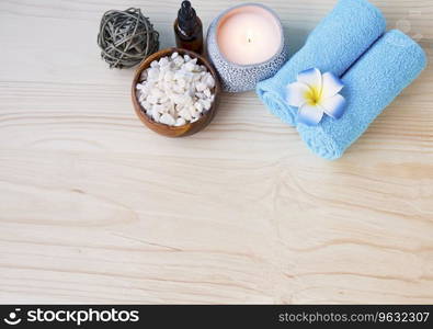 Spa setting still life with towel, frangipani towels , candle and bath salt on wooden background top view