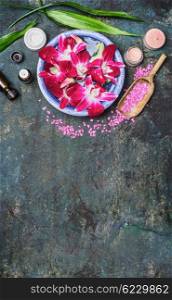 Spa setting with water bowls , pink orchid flowers ,sea salt, cosmetic cream and essential oil on dark rustic background , top view, place for text, vertical. Wellness concept