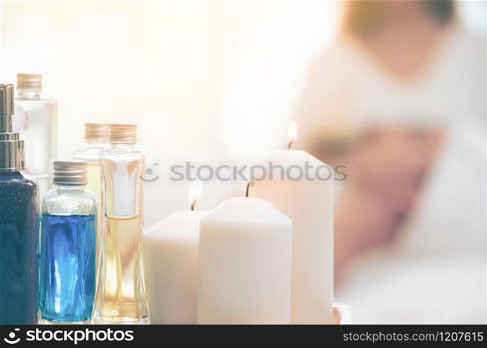 Spa treatment set including aromatic massage oil, body lotion, candle and herbal extract on a massage bed with backgrounds of woman lying on spa bed for getting spa massage.