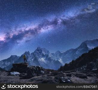 Space with Milky Way and mountains. Standing man on the stone, mountains and starry sky at night in Nepal. Rocks with snowy peaks against sky with stars. Trekking.Night landscape with bright milky way. Space with Milky Way, man on the stone and mountains