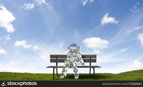 Spaceman is sitting on wooden bench. Mixed media. Astronaut in spacesuit on bench. Mixed media