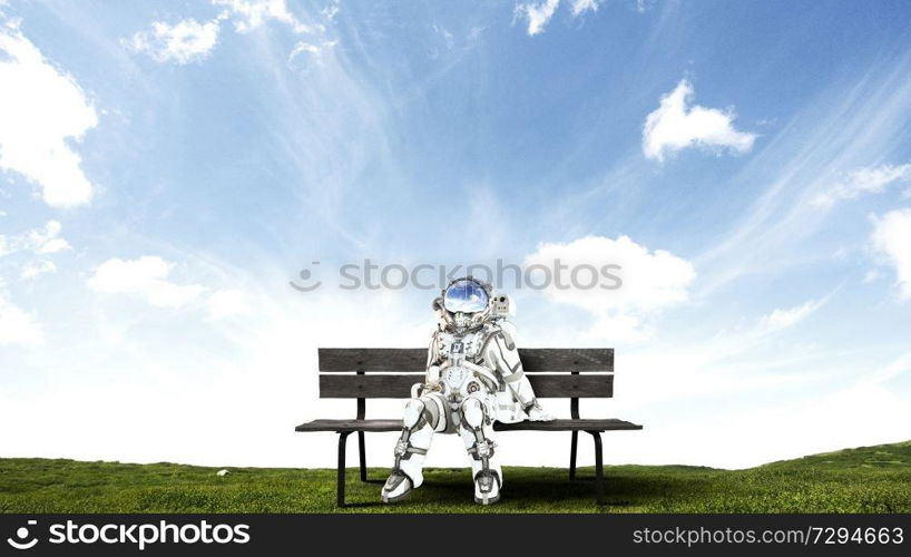 Spaceman is sitting on wooden bench. Mixed media. Astronaut in spacesuit on bench. Mixed media
