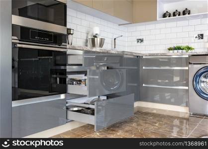 Spacious luxury well designed modern grey, beige and white kitchen with marble tiles floor, some drawers are open. Luxury modern white, beige and grey kitchen interior