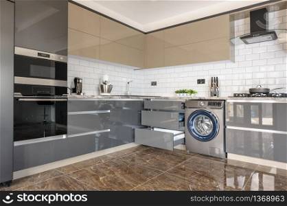 Spacious luxury well designed modern grey, beige and white kitchen with marble tiles floor. some lockers and door of electric oven are open. Luxury modern white, beige and grey kitchen interior