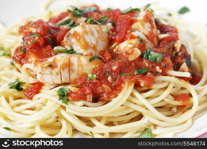 Spaghetti all&rsquo;arrabbiata with fish, garnished with parsley, seen closeup form the side. The sauce is made from tomato, garlic, olive oil and flaked chillis.