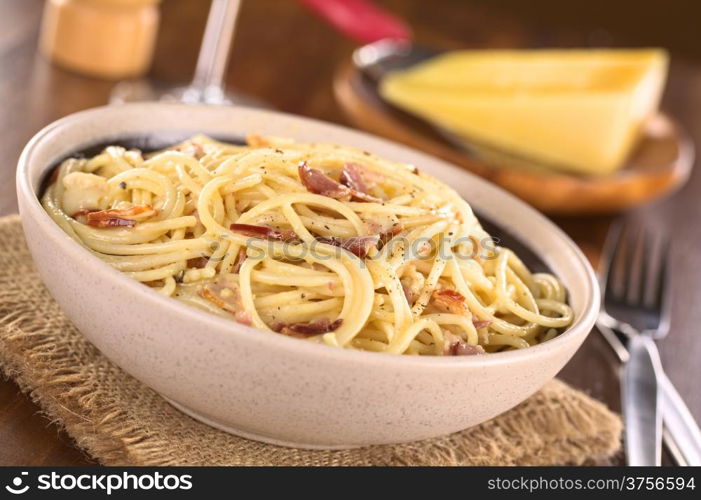 Spaghetti alla Carbonara made with bacon, eggs, cheese and black pepper served in bowl with cheese to grate in the back (Selective Focus, Focus one third into the meal)