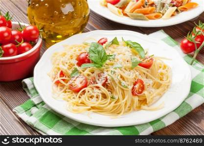 Spaghetti and penne pasta with tomatoes and basil on wooden table