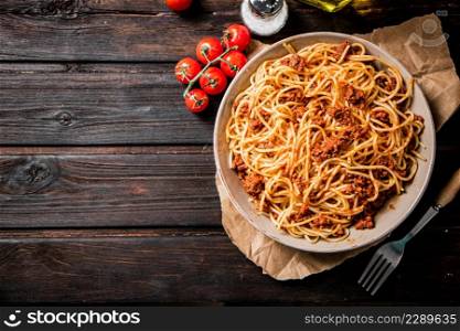 Spaghetti bolognese in a plate on a table with tomatoes. On a wooden background. High quality photo. Spaghetti bolognese in a plate on a table with tomatoes.