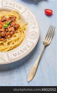 spaghetti bolognese in plate with the inscription : pasta and fork on blue wooden background, close up