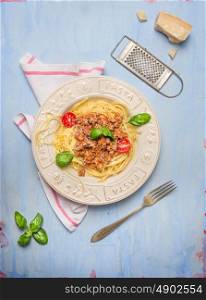 Spaghetti bolognese with fork and old parmesan grater on blue wooden background, top view