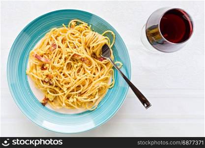 Spaghetti carbonara on with egg, smoked bacon and cheese over a table with a red wine glass seen from above. Italian spaghetti carbonara
