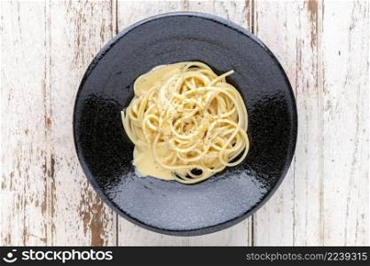 spaghetti carbonara with cream sauce and oregano on top in black ceramic plate on white old wood texture background, top view