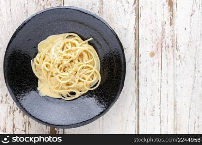 spaghetti carbonara with cream sauce and oregano on top in black ceramic plate on white old wood texture background with copy space for text, top view