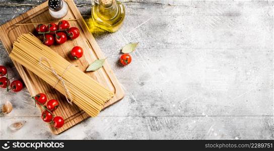 Spaghetti dry on a wooden cutting board with tomatoes. On a gray background. High quality photo. Spaghetti dry on a wooden cutting board with tomatoes.