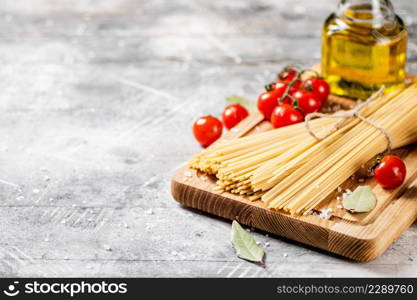 Spaghetti dry on a wooden cutting board with tomatoes. On a gray background. High quality photo. Spaghetti dry on a wooden cutting board with tomatoes.